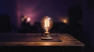 Leuchtende Glühlampe auf dunklem Hintergrund neben einer Tischkante